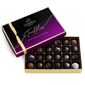 Godiva dark chocolate truffles in a purple and black box with a yellow ribbon, featuring an assortment of varied designs and textures.