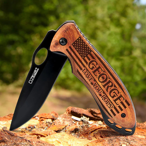 A folding pocket knife with a black blade and wooden handle engraved with \“George\“ and \“Love You Pops,\“ along with an American flag design.