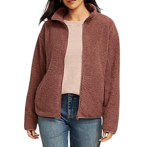 A woman is wearing a mauve zip-up textured fleece jacket over a light pink top and blue jeans.