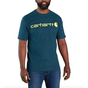 A man is wearing a teal Carhartt T-shirt with yellow logo text across the chest, paired with blue jeans.