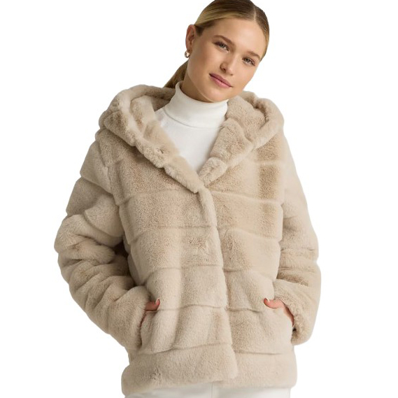 A woman is wearing a light beige faux fur hooded jacket with horizontal stripe patterns over a white turtleneck sweater.