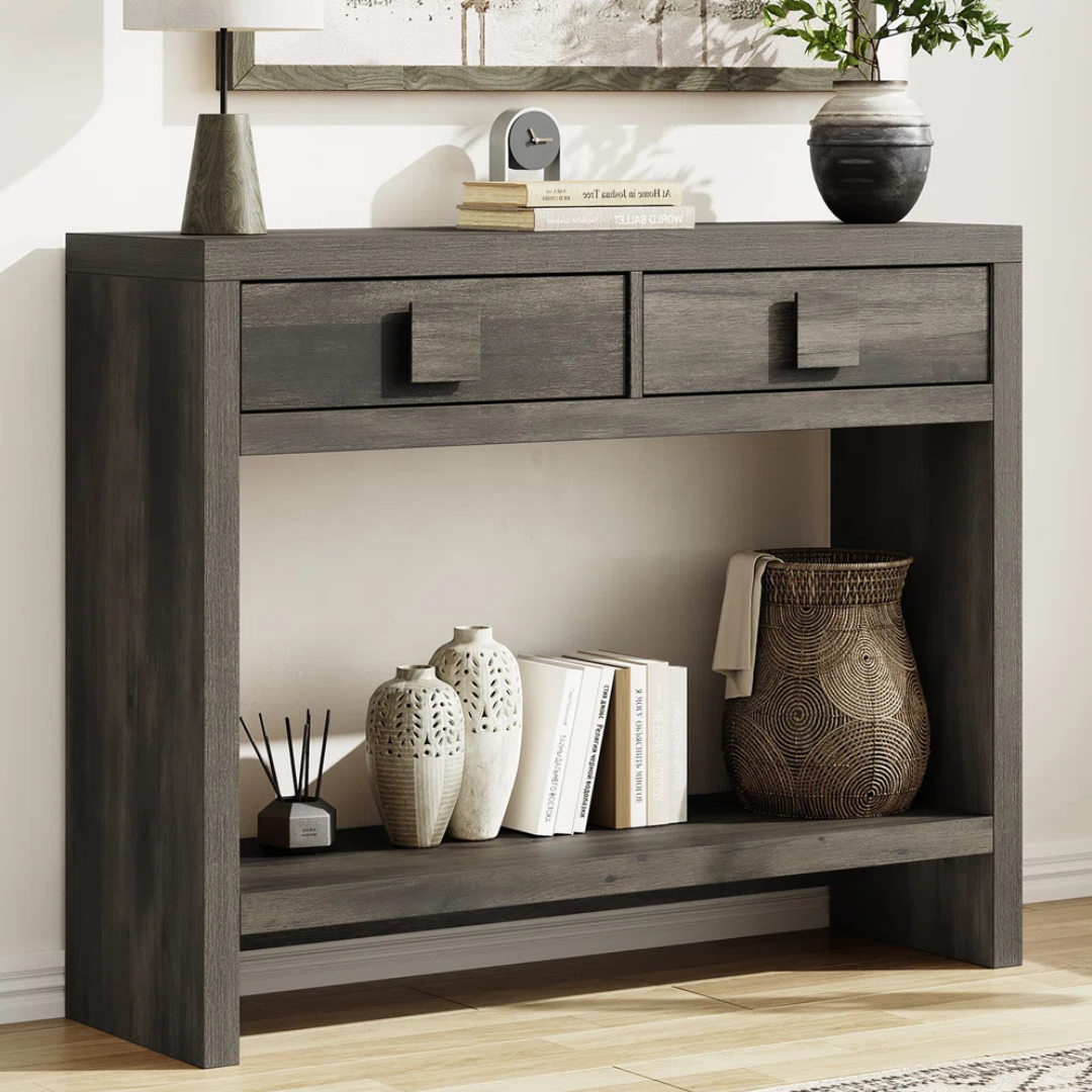 Dark wood console table with two drawers, displaying decorative vases, books, a wicker basket, and a small clock.