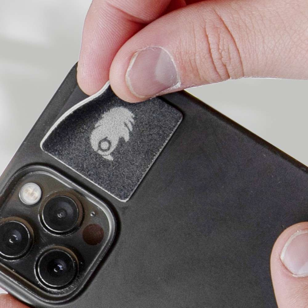 A person is peeling off a square sticker designed to cover the rear camera lenses on a smartphone for protection or privacy.