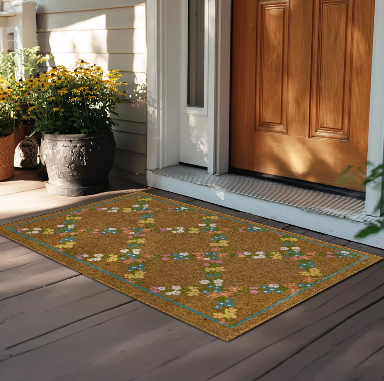A decorative doormat with a floral pattern lies at the entrance of a wooden door. A large pot of yellow flowers is to the side, enhancing the welcoming appearance of the porch area.
