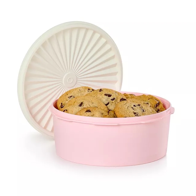 A pink Tupperware 7.5 Cup Cookie Canister with a white lid featuring a fluted design, filled with chocolate chip cookies.