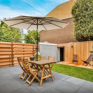9' patio umbrella with a round beige canopy and dark wooden frame, providing shade over a wooden outdoor dining set on a tiled patio.