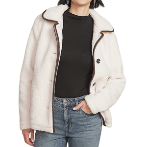 A woman is wearing a white, fleece-lined jacket with dark trim, a black high-neck top, and blue jeans.