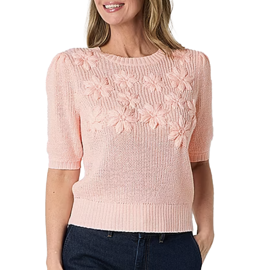 Light pink knit floral sweater top with short sleeves, features a floral pattern on the chest. Ribbed hem and sleeves add a classic touch. Worn with dark jeans.