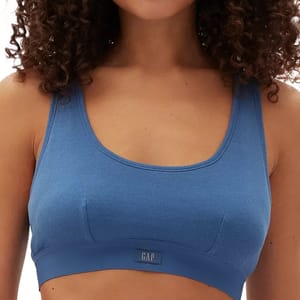 A woman wears a blue Gap Comfort Bralette featuring a scoop neckline and ribbed fabric with a logo tag on the front.