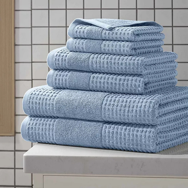 A stack of light blue towels with a waffle texture, neatly placed on a countertop in a tiled bathroom setting.