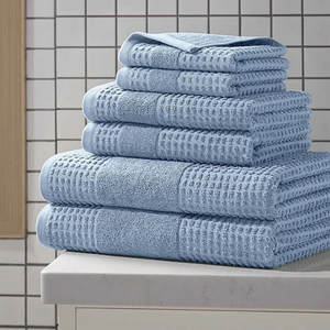 A stack of light blue towels with a waffle texture, neatly placed on a countertop in a tiled bathroom setting.