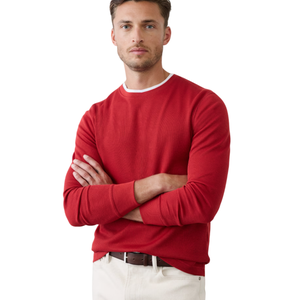 A man is wearing a red long-sleeve shirt with a white crew neck and off-white pants secured with a brown belt.