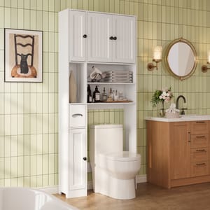Bathroom setup with a white over-the-toilet storage unit featuring shelves and cabinets, a toilet, a wood vanity with a sink, and a round mirror. The green tiled wall includes a chair-themed art piece and wall sconces.