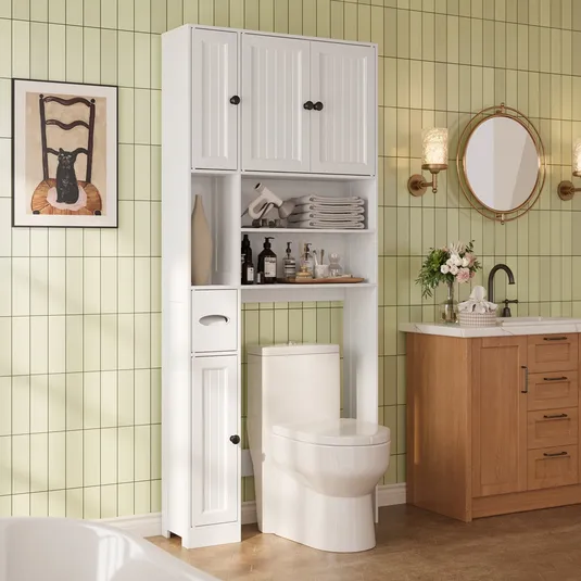 Bathroom setup with a white over-the-toilet storage unit featuring shelves and cabinets, a toilet, a wood vanity with a sink, and a round mirror. The green tiled wall includes a chair-themed art piece and wall sconces.