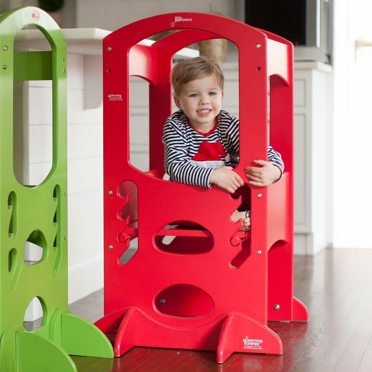 A red children's step stool with a safety rail, designed to help kids reach higher surfaces. It features a stable base and cut-out shapes on the sides for additional support.
