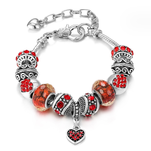 A silver bracelet with ornamental beads and red accents, featuring a dangling heart charm with red stones.