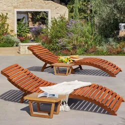 Two curved wooden lounge chairs with a small wooden table are set on a patio, surrounded by lush garden greenery.