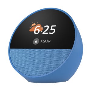 A blue Echo Spot smart alarm clock with a round display shows the time, weather, and alarm settings. It has a front-facing speaker and a sleek, compact design.
