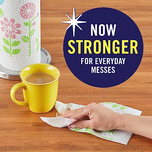 A roll of Sparkle paper towels with a floral pattern is shown beside a yellow mug, with a hand wiping a surface using a sheet. Text indicates the towels are now stronger for everyday messes.