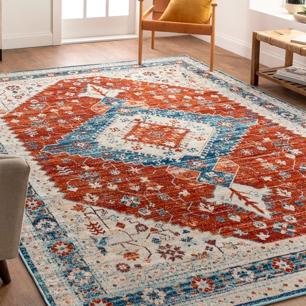 Bungalow Rose indoor/outdoor rug features a bold geometric design with red and blue patterns on a cream background, suitable for both indoor and outdoor use.