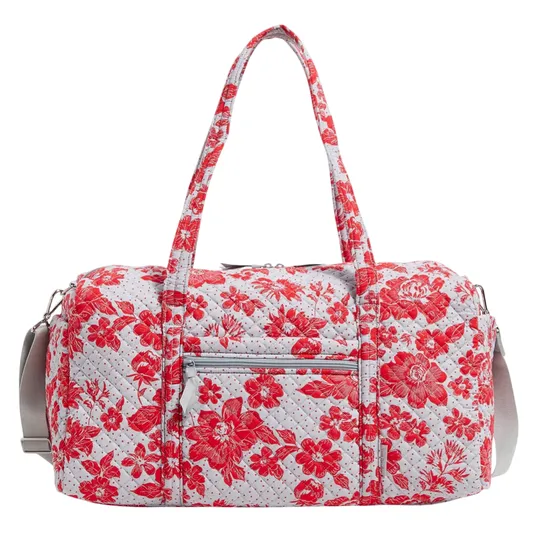 A quilted floral-patterned duffel bag featuring red flowers on a white background, equipped with dual handles, a detachable shoulder strap, and a front zip pocket.