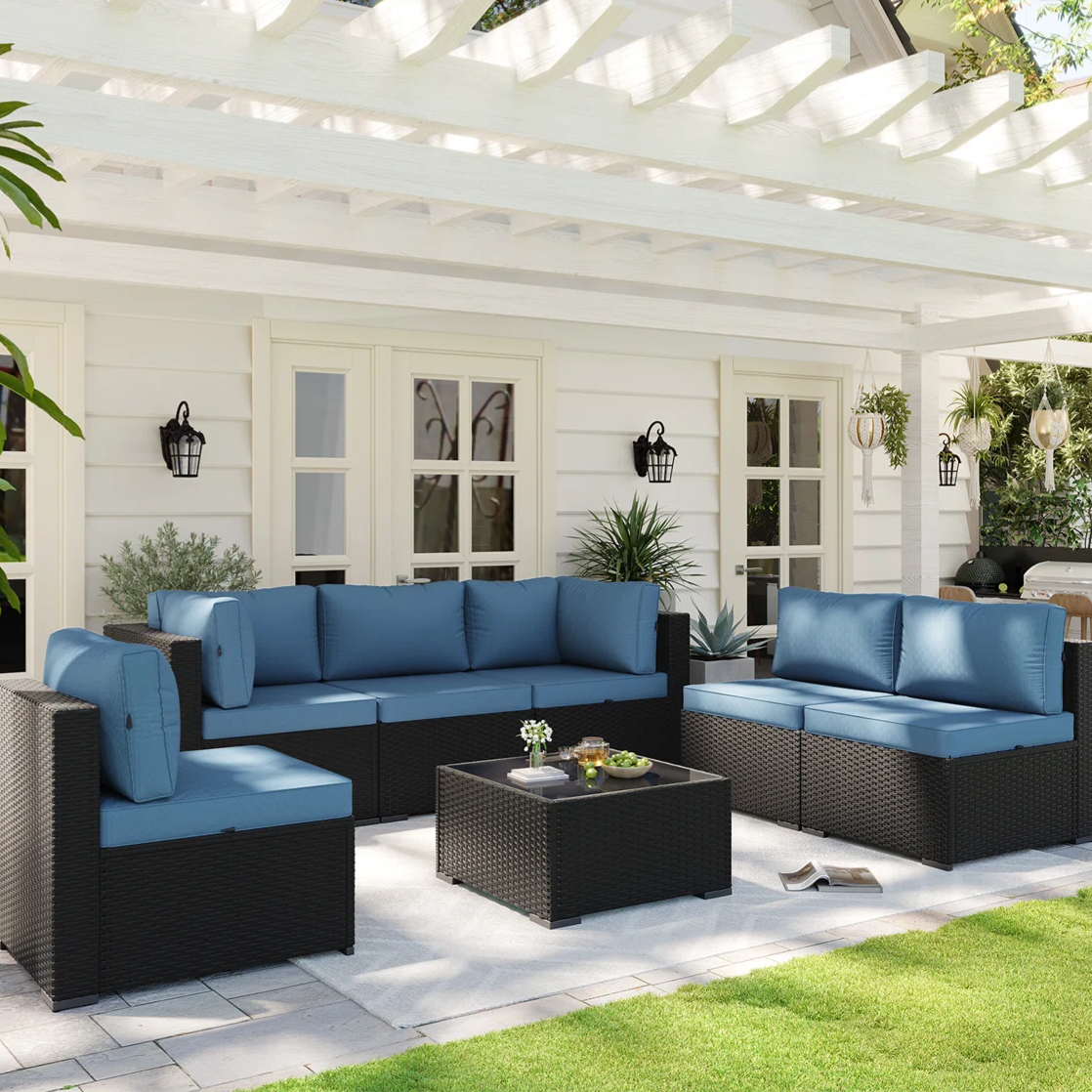 Outdoor patio furniture set with blue cushions and black wicker base, featuring a sofa, chairs, and a coffee table, set on a tiled patio beneath a white pergola.