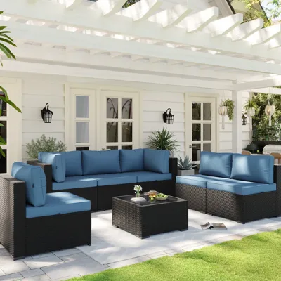 Outdoor patio furniture set with blue cushions and black wicker base, featuring a sofa, chairs, and a coffee table, set on a tiled patio beneath a white pergola.