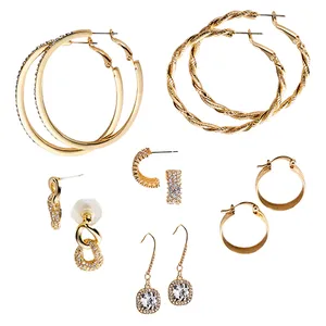 A set of gold-toned earrings featuring two pairs of large hoop earrings, a twisted rope design, and a thick smooth design. Includes smaller hoops, crystal-accented studs, and a pair of dangle earrings with clear gemstones.