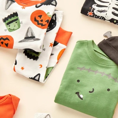 A selection of baby clothes with Halloween-themed designs, including a green shirt with a friendly Frankenstein face.