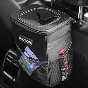 A black car trash can with a flip-top lid is hanging on the back of a car seat, featuring side mesh pockets and a white and red logo on the front.