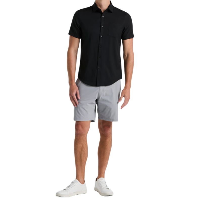 Limitless Stretch Tech Shorts are light gray, knee-length, and feature a relaxed fit with a smooth texture, designed for comfort and flexibility. They're paired with a black short-sleeved shirt and white sneakers in the outfit shown.