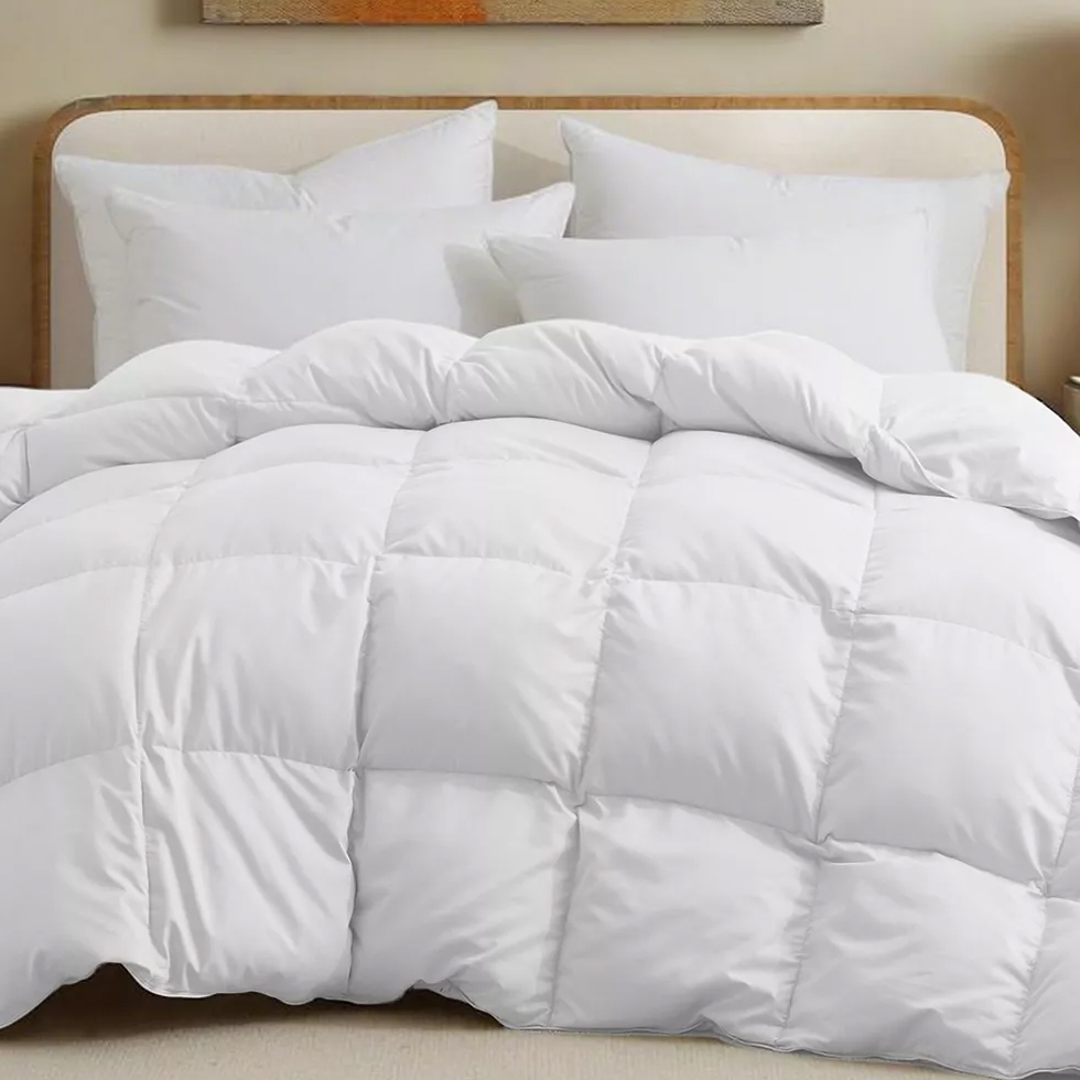 A white, quilted comforter is displayed on a bed with multiple white pillows in the background.