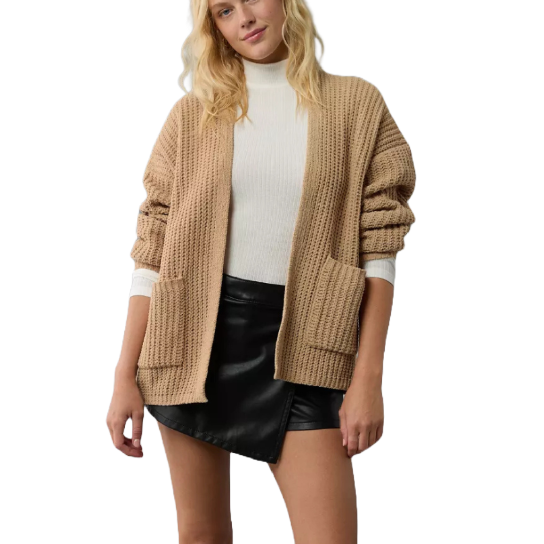 A beige, waffle-knit open cardigan with long sleeves and two front pockets, worn over a white turtleneck.