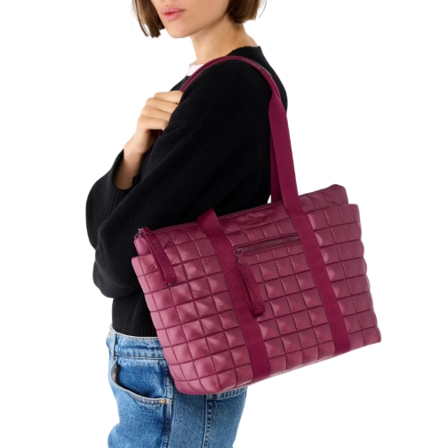 A woman carries a quilted, deep pink shoulder bag with long straps, wearing a black top and blue jeans.