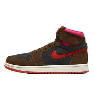 The Air Jordan 1 Zoom CMFT 2 features a high-top design with brown suede overlays, a dark gray base, and red accents, including the Nike Swoosh. It includes a pink collar and a white midsole with a red outsole for contrast.