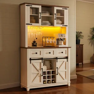 A white wooden hutch with sliding barn doors features a coffee machine, hanging wine glasses, and shelves for dishes and wine bottles, highlighted by warm lighting.