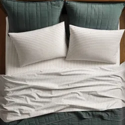 A bed is made with green quilted pillow shams and a matching blanket, alongside striped white pillowcases and sheets.