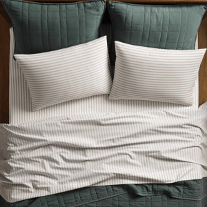 A bed is made with green quilted pillow shams and a matching blanket, alongside striped white pillowcases and sheets.