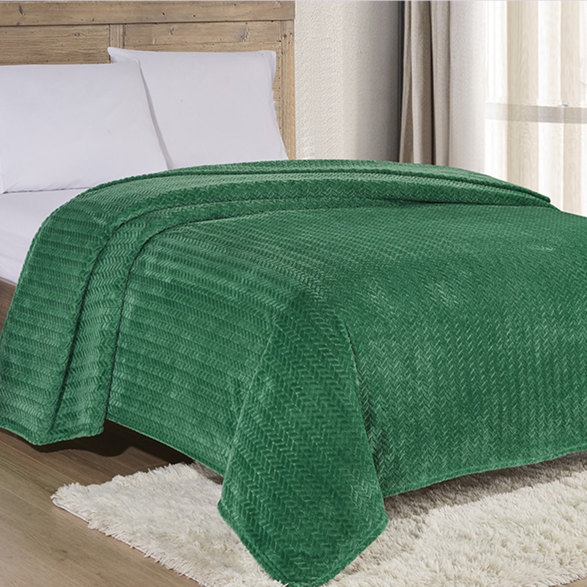 A green textured bedspread covers a bed with white pillows, set on a wooden floor with a light-colored rug nearby.