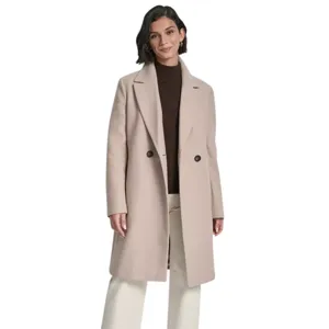 A woman is wearing a long beige coat with two buttons over a brown turtleneck sweater, paired with cream-colored wide-leg pants and dark ankle boots.