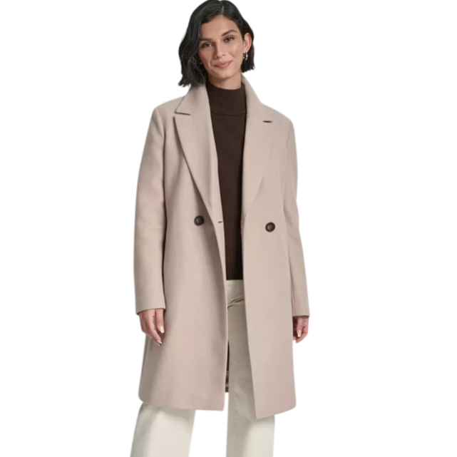 A woman is wearing a long beige coat with two buttons over a brown turtleneck sweater, paired with cream-colored wide-leg pants and dark ankle boots.