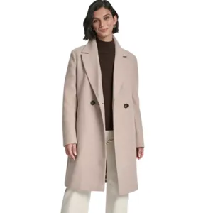 A woman is wearing a long beige coat with two buttons over a brown turtleneck sweater, paired with cream-colored wide-leg pants and dark ankle boots.