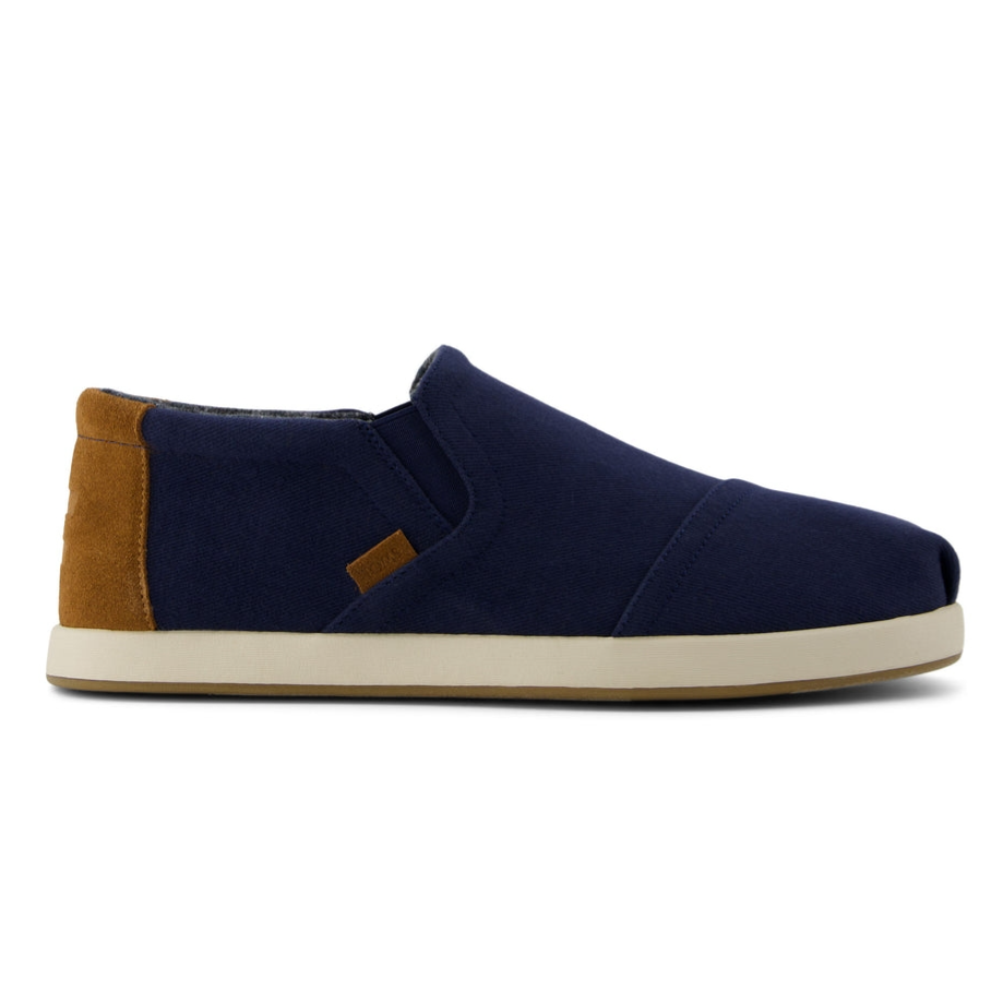 A pair of slip-on shoes with a navy blue canvas upper, brown heel accents, and white rubber sole.