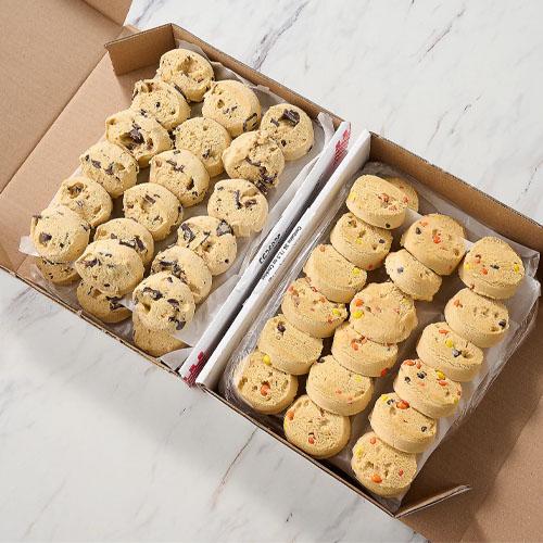 Two varieties of cookie dough are arranged in scoops inside a box, one with chocolate chunks and the other with colorful candy pieces.