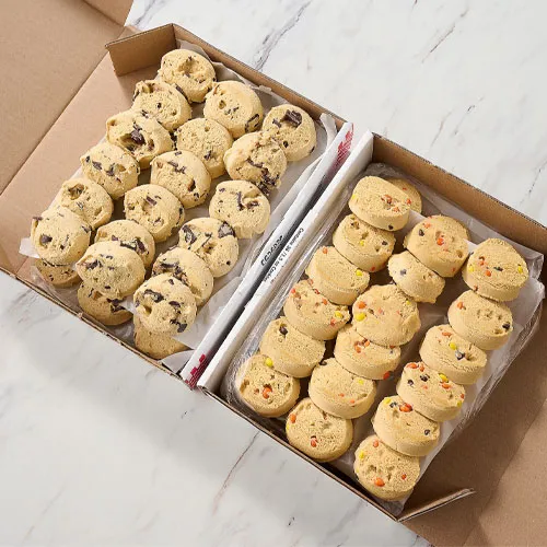 Two varieties of cookie dough are arranged in scoops inside a box, one with chocolate chunks and the other with colorful candy pieces.