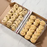 Two varieties of cookie dough are arranged in scoops inside a box, one with chocolate chunks and the other with colorful candy pieces.