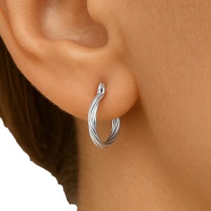 A close-up of an ear wearing a twisted silver hoop earring, designed with a sleek, intertwined metal pattern.