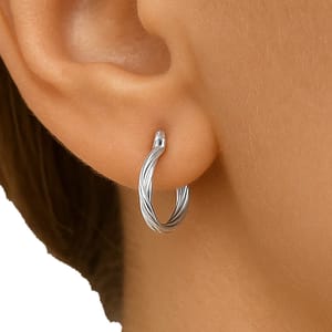 A close-up of an ear wearing a twisted silver hoop earring, designed with a sleek, intertwined metal pattern.