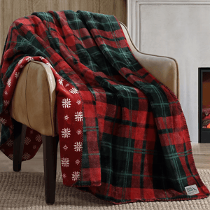 A cozy plaid blanket with red and green colors draped over a leather armchair. It features a snowflake design on the reverse side.