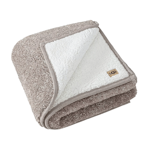 A cozy, folded blanket with a textured gray outer layer and a soft white sherpa lining, featuring a small \“UGG\“ logo tag on the corner.